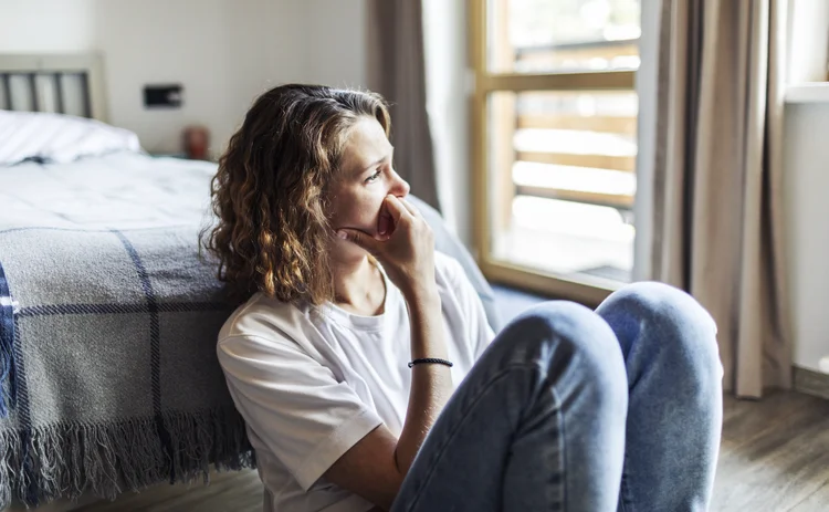 Young adult woman with depression sitting at home alone